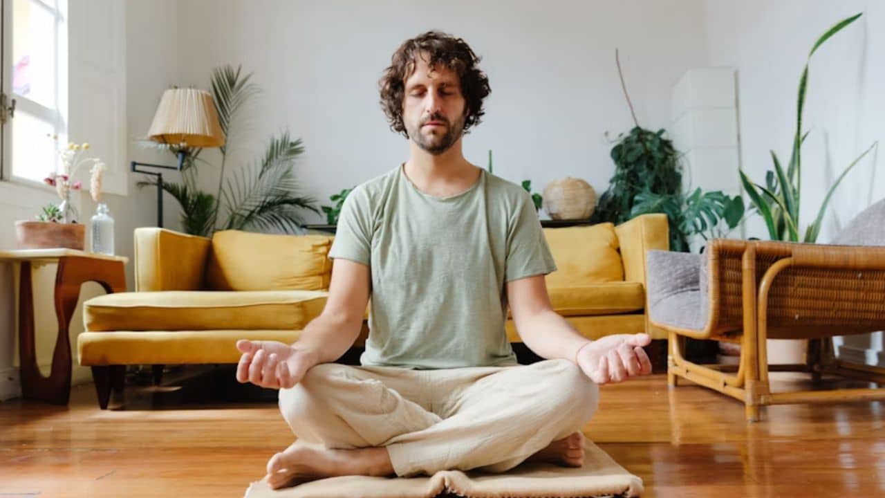 Man meditating on a yoga mat in his living room.