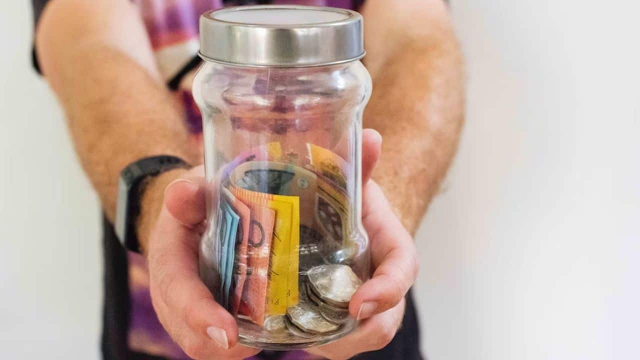 Man holding a jar of coins and bills.