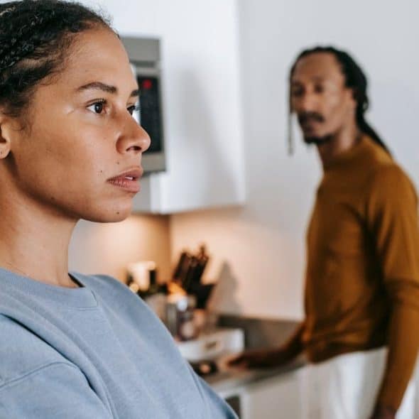 A frustrated woman is in the foreground, with a man looking at her in the background.