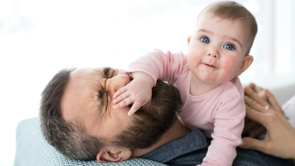 A happy baby is lying on its father, who is smiling with a squeezed face.