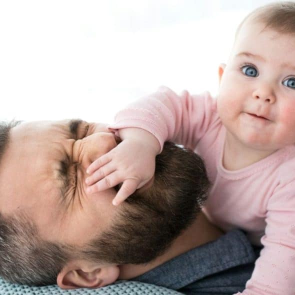 A happy baby is lying on its father, who is smiling with a squeezed face.