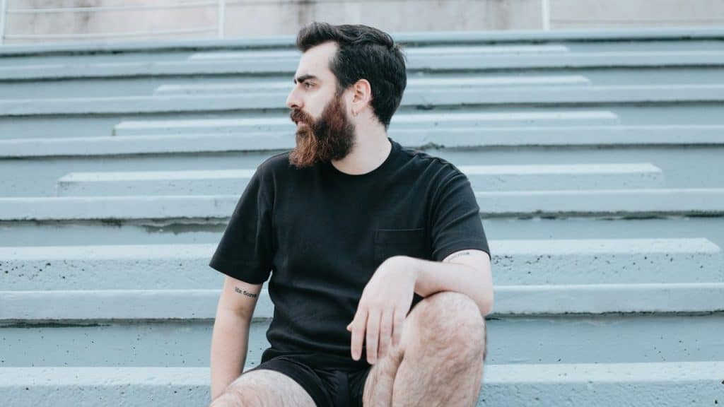 A worried man with a beard is looking away while sitting on concrete stairs