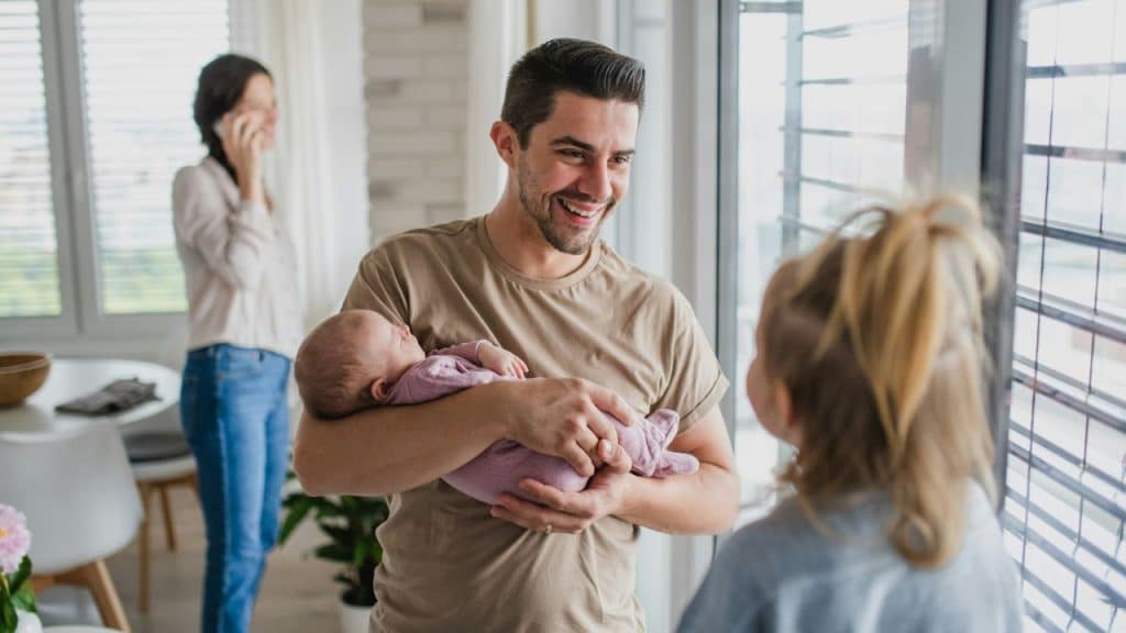 A happy family is at home. A father holds a baby, looking at his daughter.