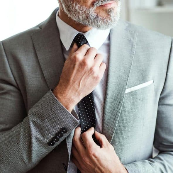 A man in a gray suit adjusting his black polka dot tie.