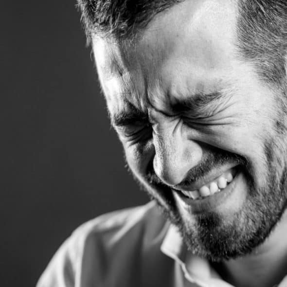 A black-and-white close-up of a man with a beard, smiling with his eyes squeezed shut.