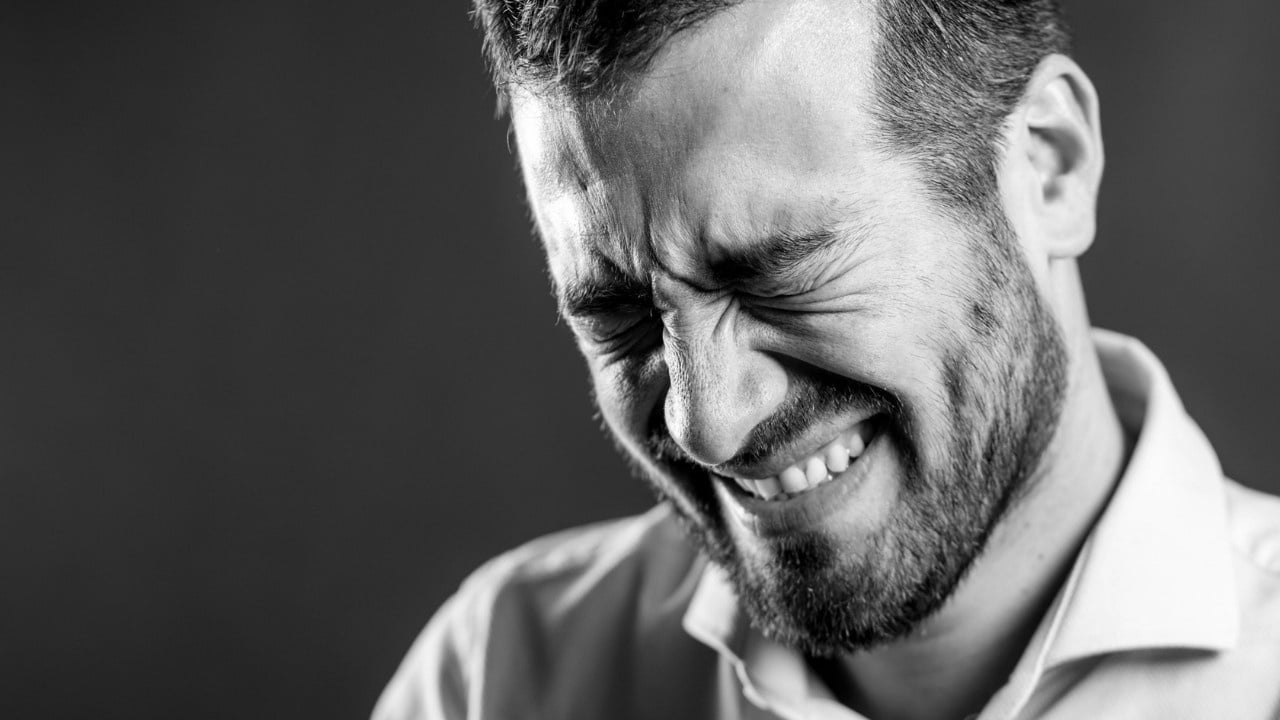 A black-and-white close-up of a man with a beard, smiling with his eyes squeezed shut.