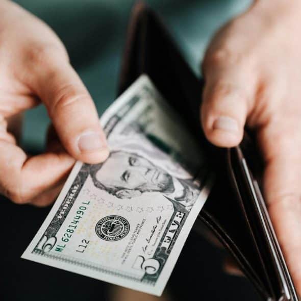 A person holding a five-dollar bill and a wallet.