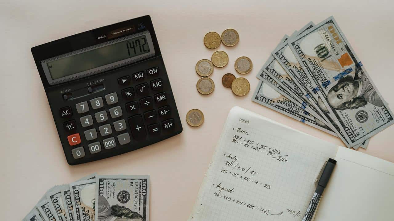 A calculator, coins, cash, and a notebook with handwritten calculations.