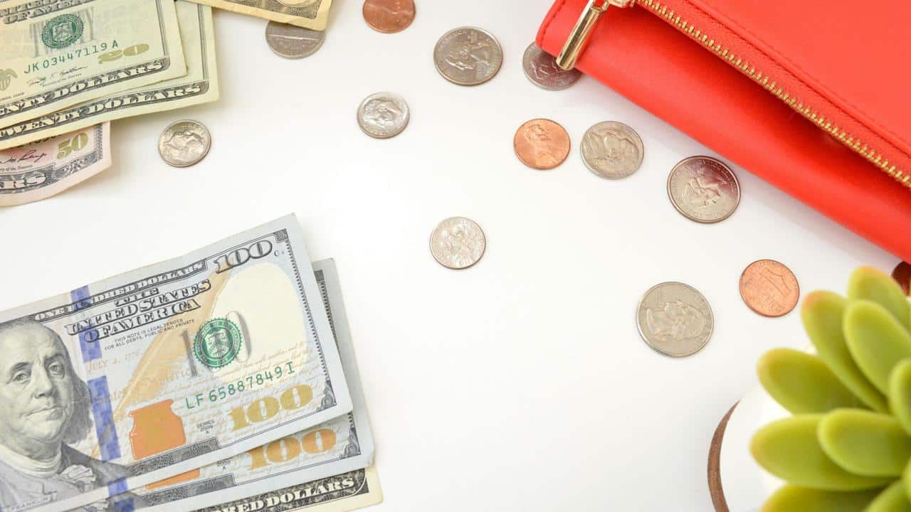 A red wallet, coins, and dollar bills on a white surface.