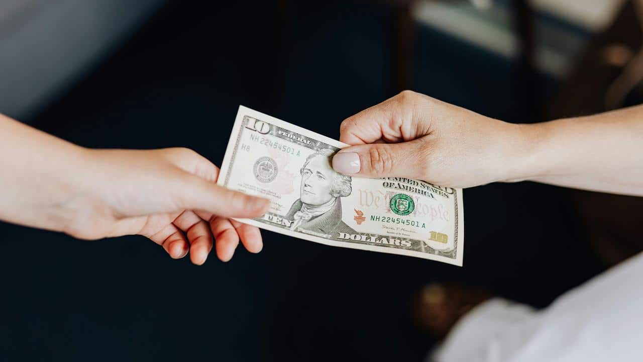 A person handing over a ten-dollar bill to someone else.