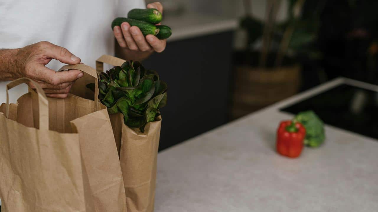 A person unpacking groceries with vegetables on a kitchen counter.
