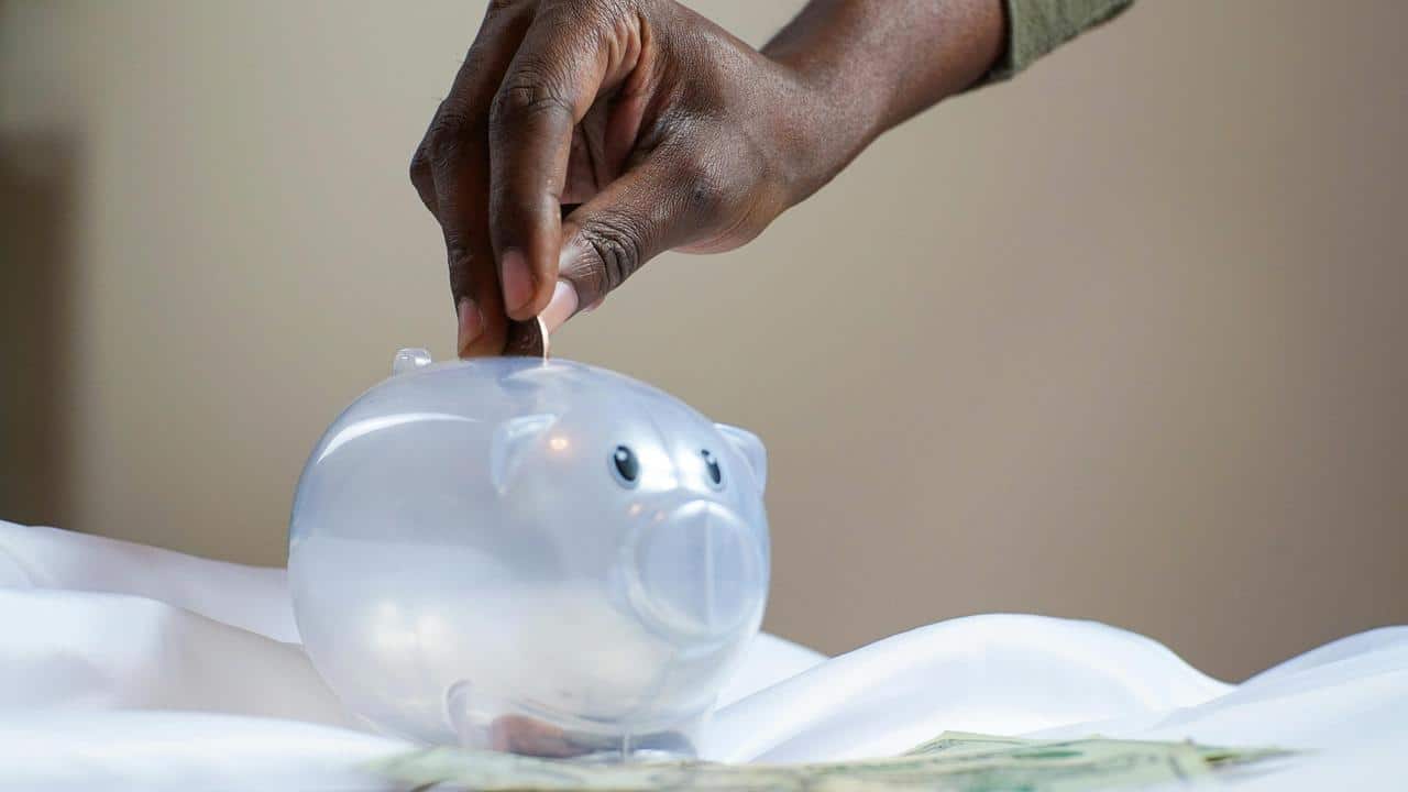 A person’s hand placing a coin into a clear piggy bank.