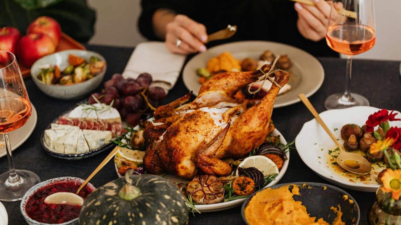 A table set with a roasted chicken, side dishes, and wine glasses.