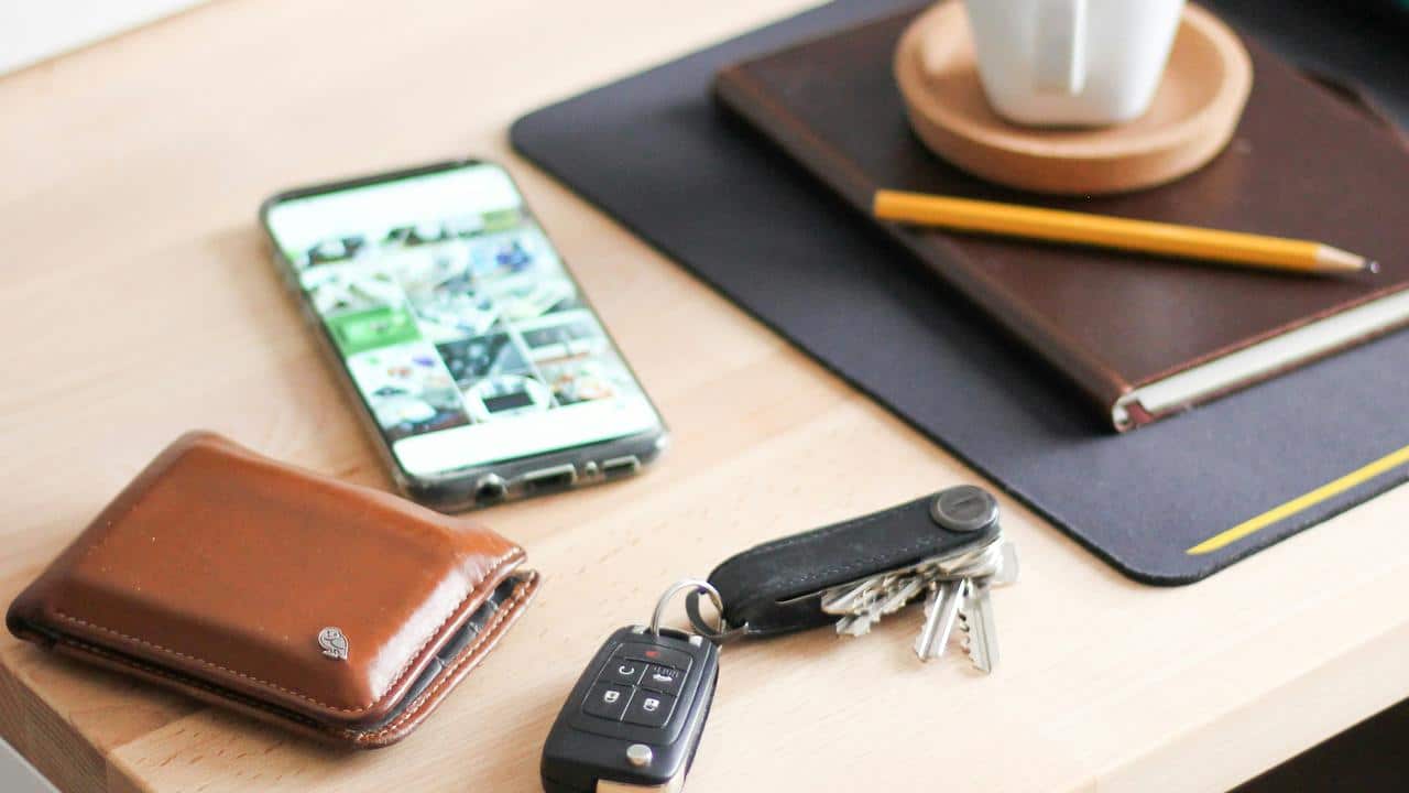 A wallet, phone, keys, and notebook on a desk.
