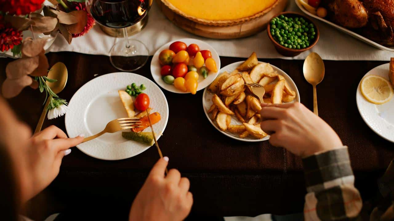 A table with people eating a meal of vegetables, potatoes, and wine.