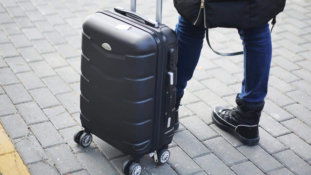 A traveler standing with a suitcase on wheels.