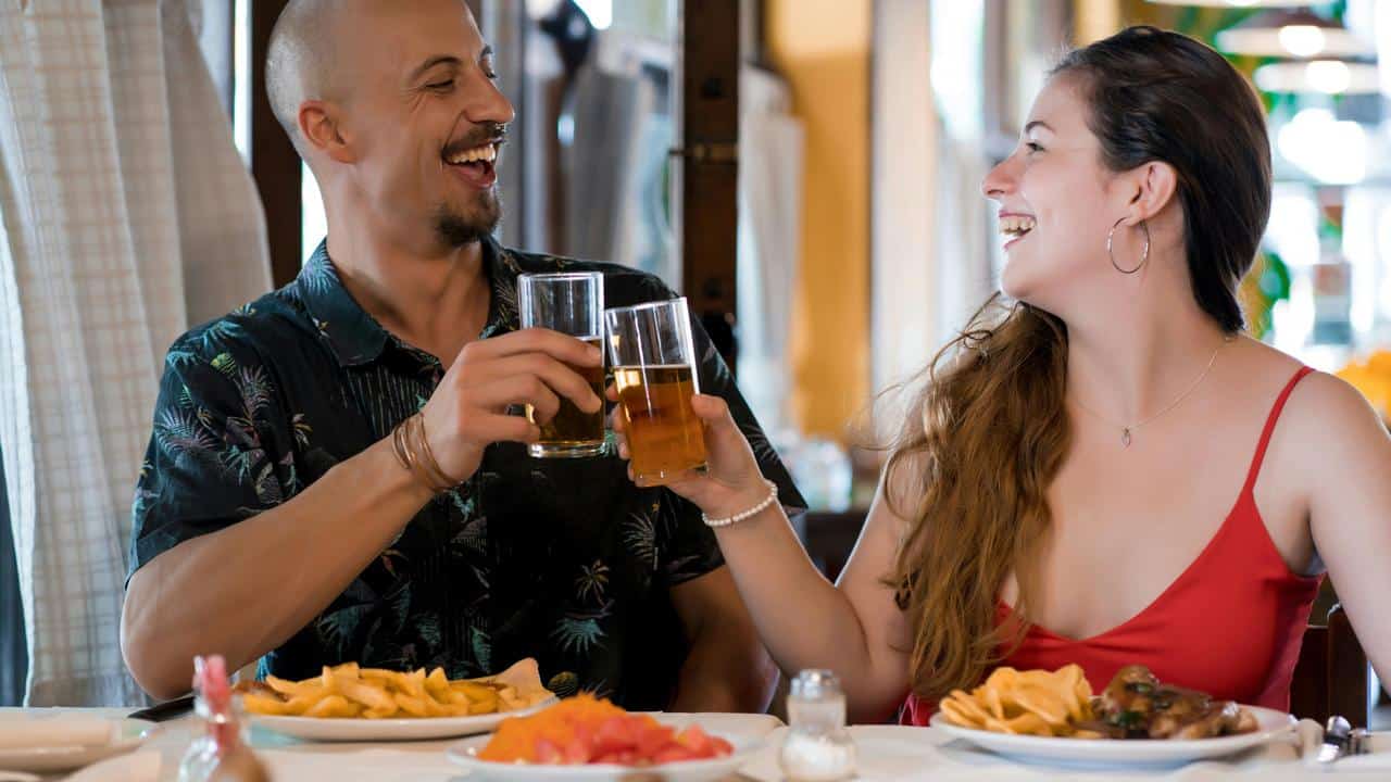 A couple smiling and clinking glasses at a restaurant table.
