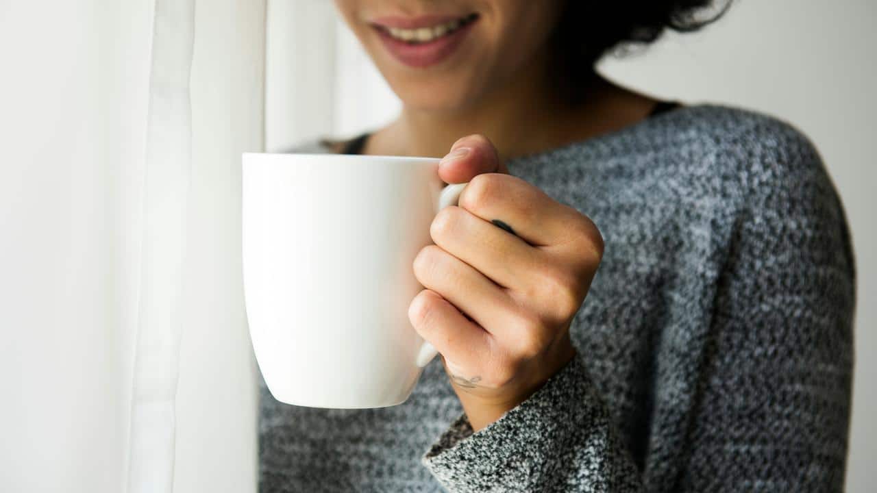 A person holding a white mug while smiling.