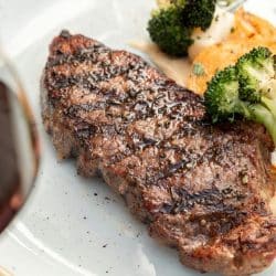 A grilled steak with broccoli, potatoes, and a glass of red wine.