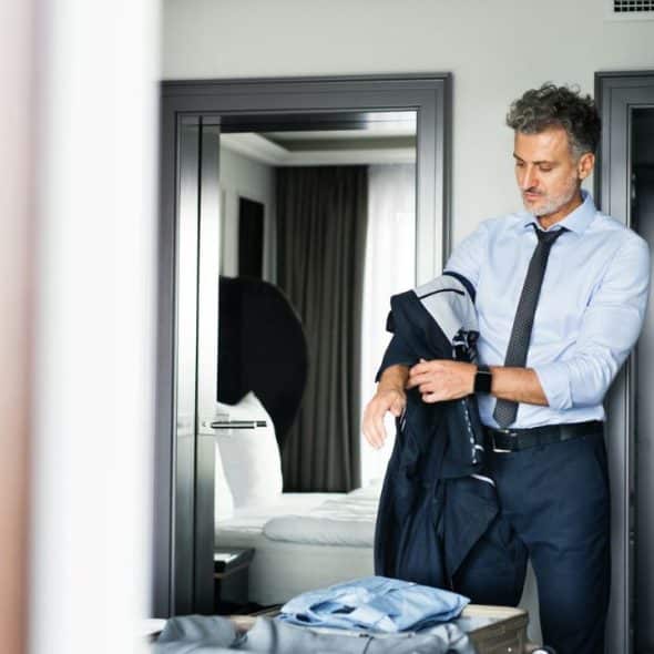A man in a tie and button-down shirt is putting on a suit jacket.