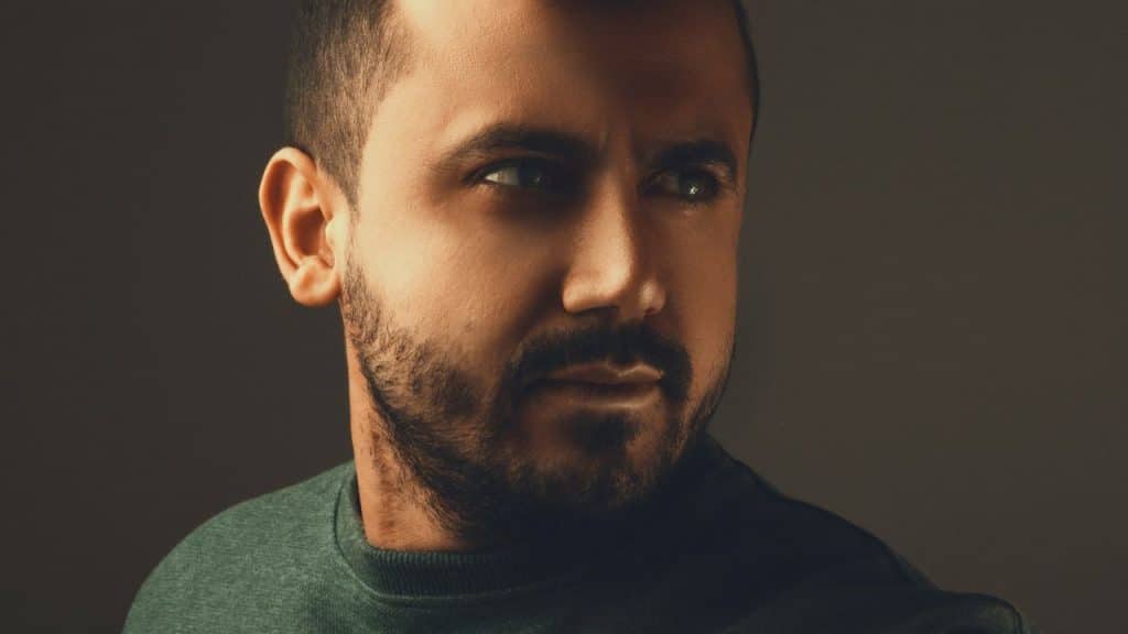 A man with a beard is looking to the side with an intense expression.