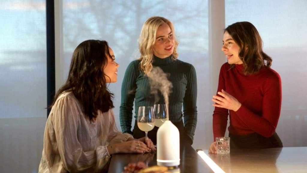 Three women are talking at a table with drinks and a white diffuser.