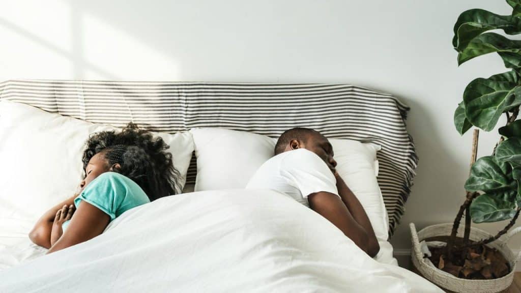 A man and a woman are sleeping in a bed with their backs to each other.