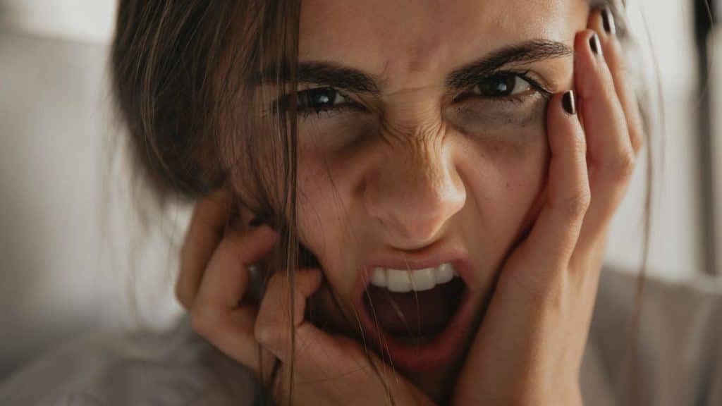 A woman with her hands on her face is screaming at the camera.