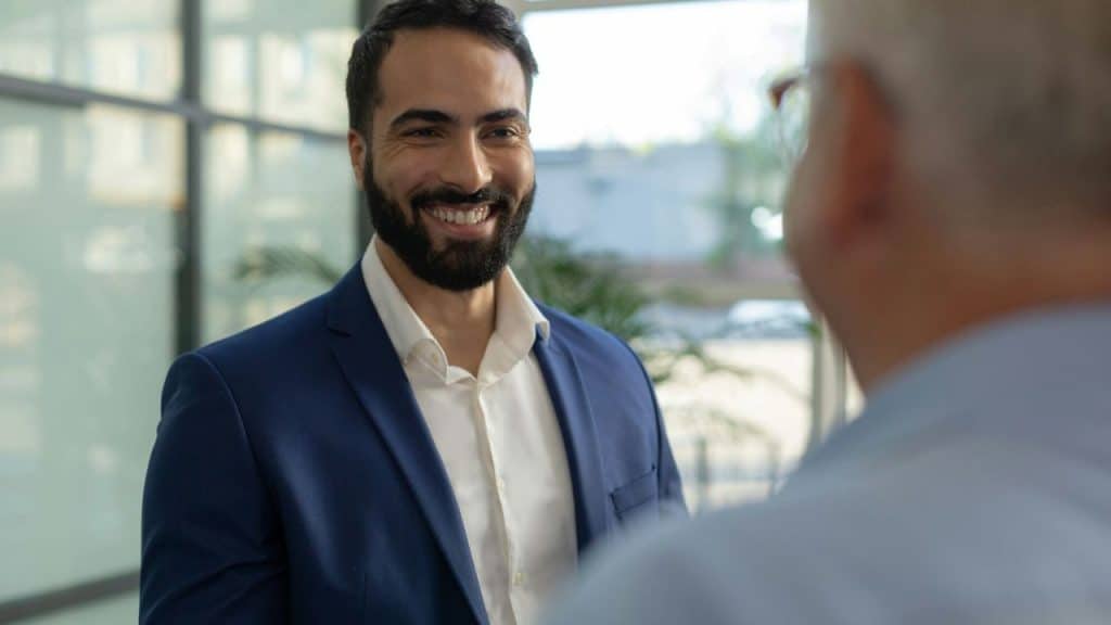 A bearded man in a blue suit and white shirt smiles at an unseen person.