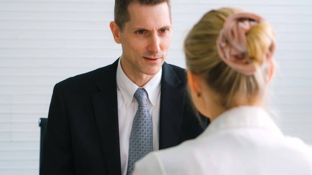 A man in a suit and tie looks intently at a woman with her back to the camera.