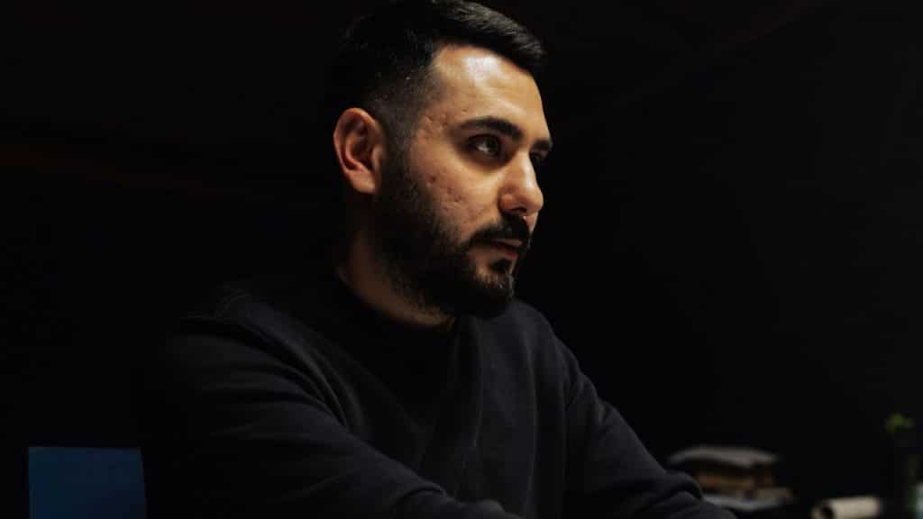 A man with a beard sits in a dark room.