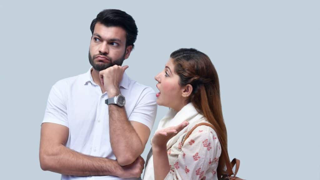 A man with his arms crossed looks away from a woman talking with her hand out.