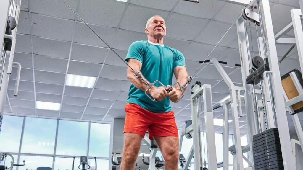 A mature man with gray hair is using a cable machine at a gym.