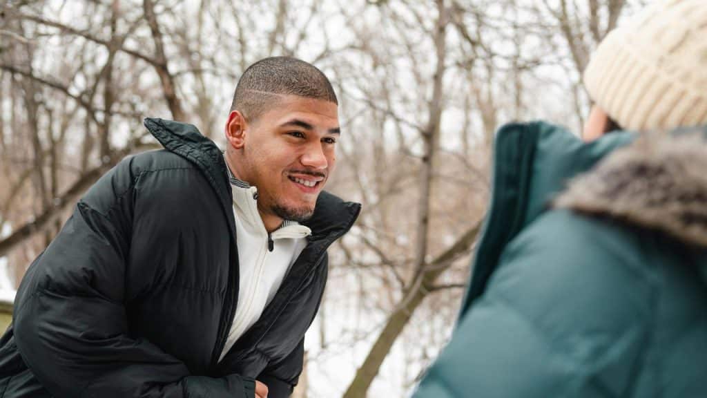 A man in a puffy winter jacket smiling outdoors.