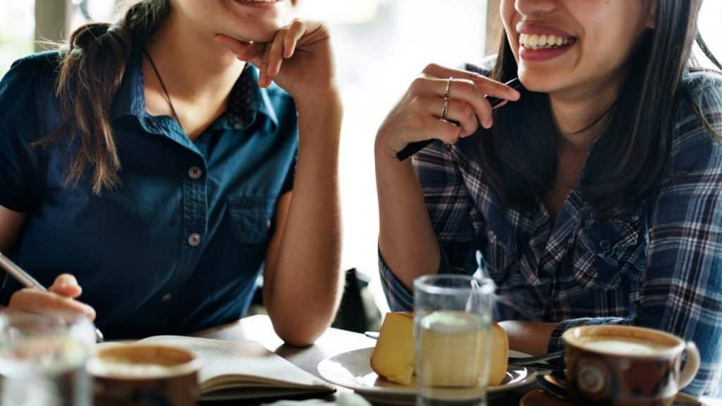 A close-up of two women smiling and chatting over coffee and dessert at a café.