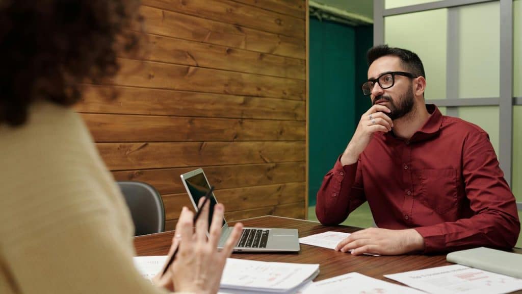 A man in a red shirt listening to a colleague during a meeting.