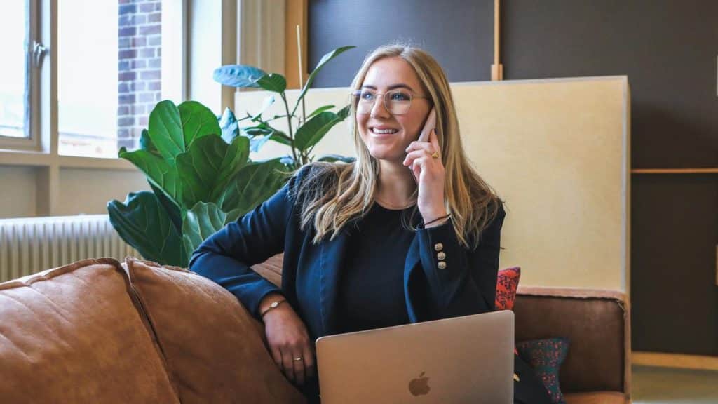 A woman smiling while talking on the phone with a laptop on her lap.