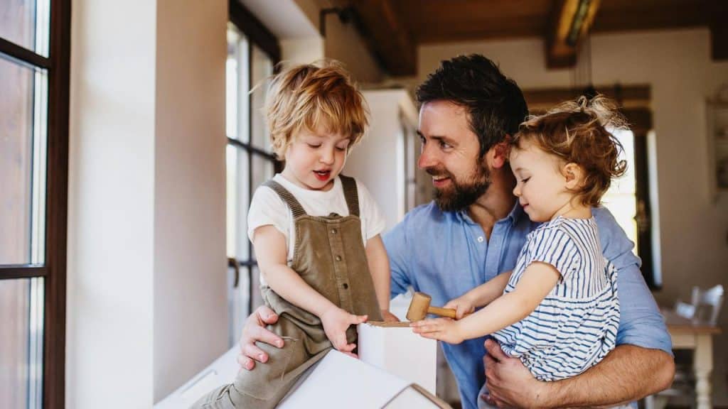 A father playing with his two young children at home.