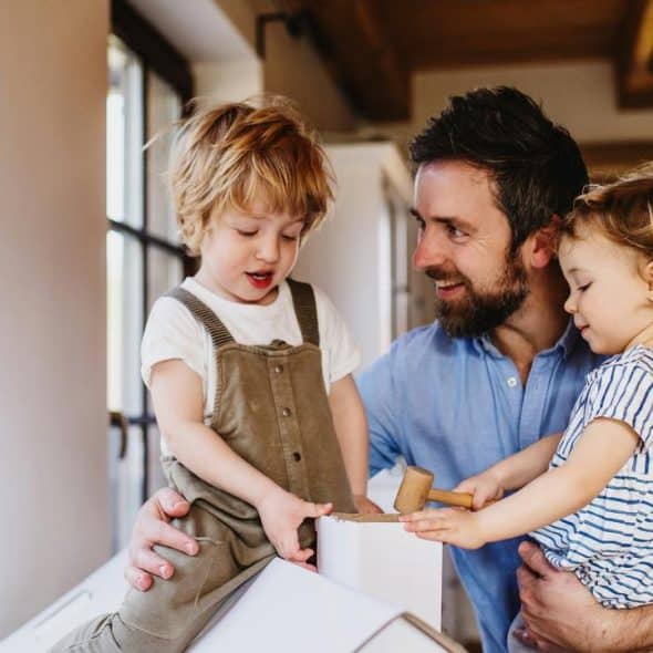 A father playing with his two young children at home.