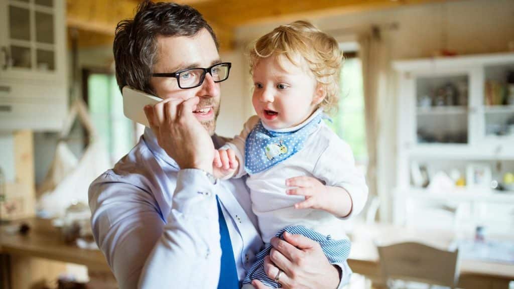 A father holding his child while talking on the phone.