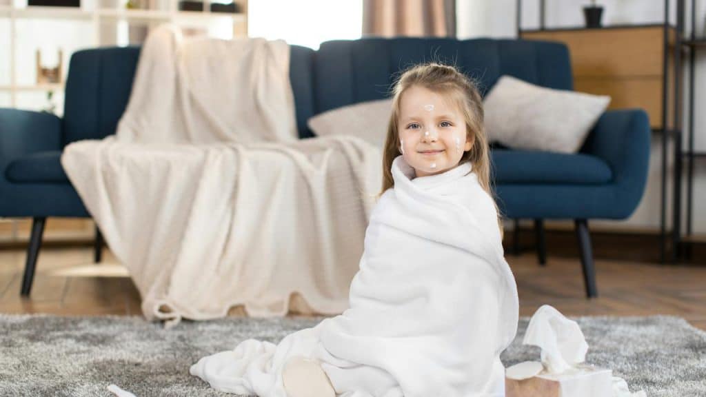 A child wrapped in a blanket with cream spots on her face.
