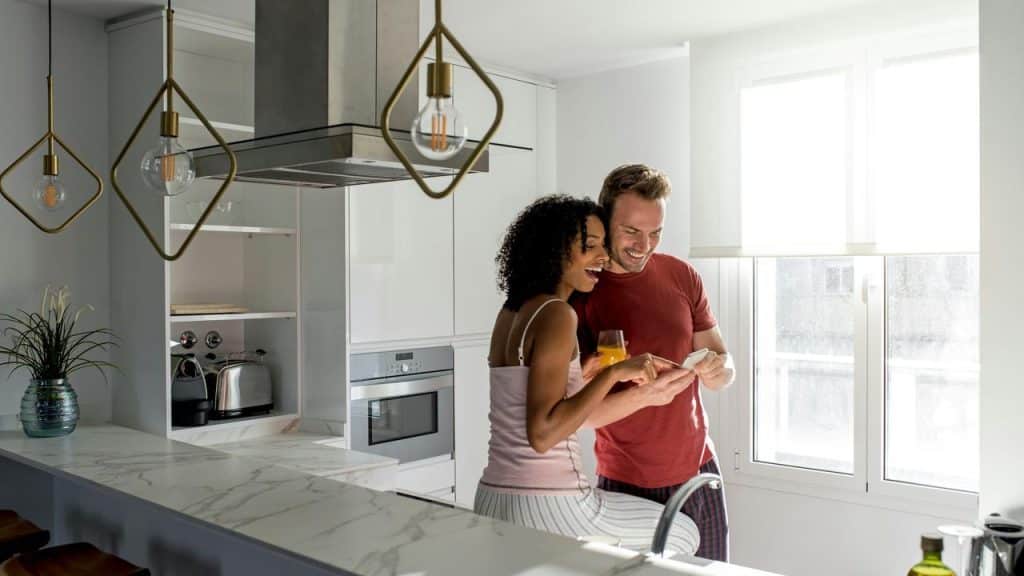 A couple smiling and looking at a phone together in the kitchen.