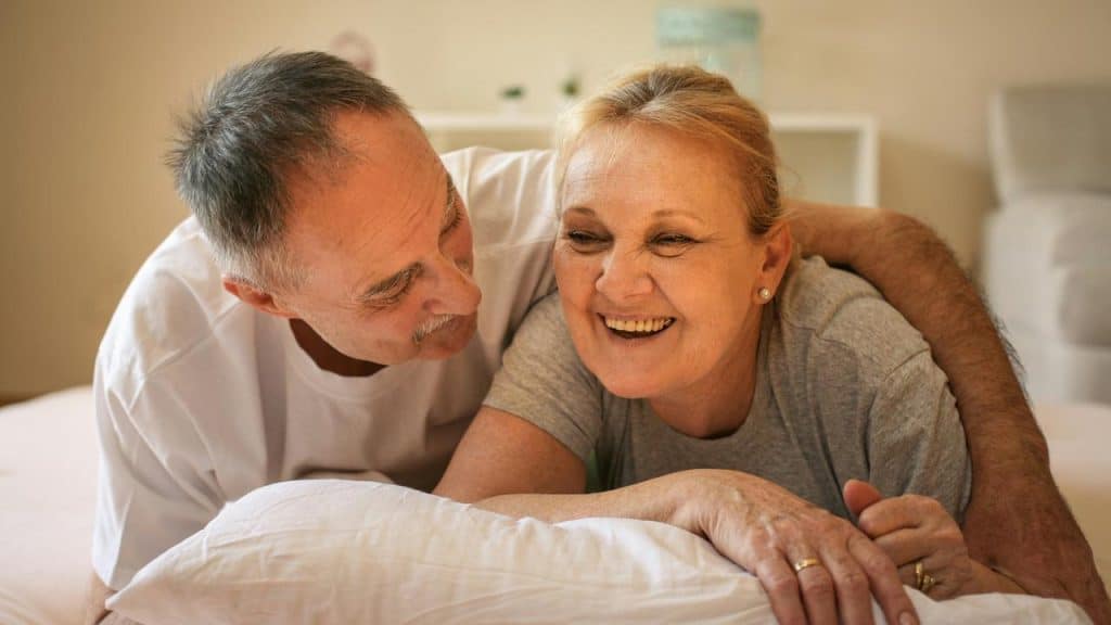 An older couple laughing together on a bed.