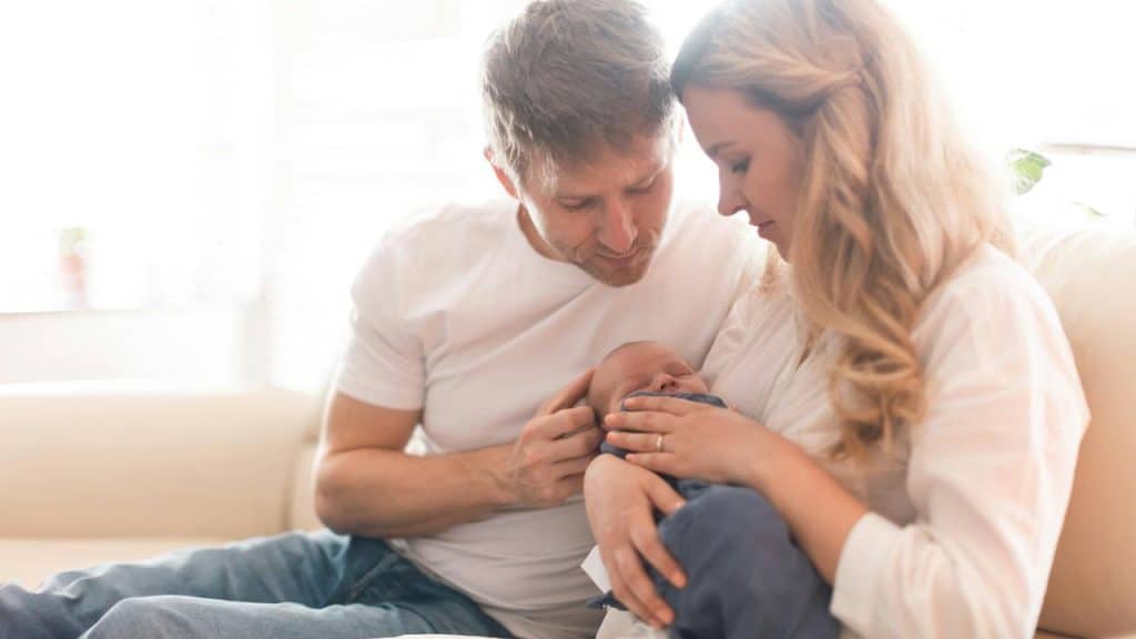 A couple sitting on a couch lovingly holding their newborn baby.