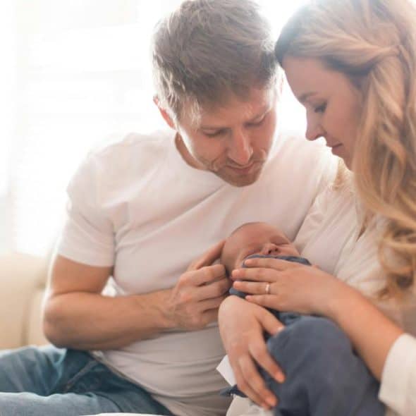 A couple sitting on a couch lovingly holding their newborn baby.