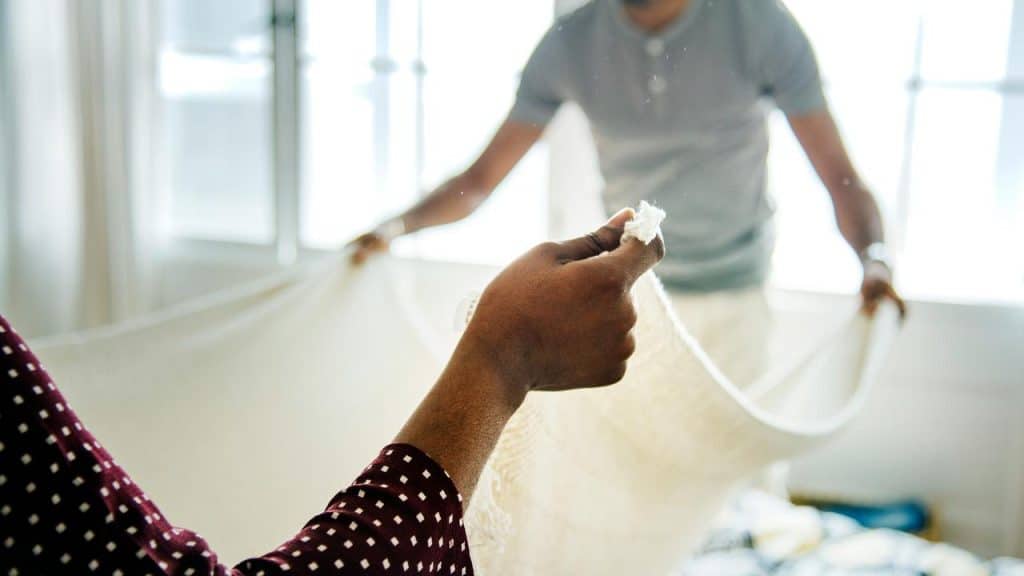 A couple making a bed together.