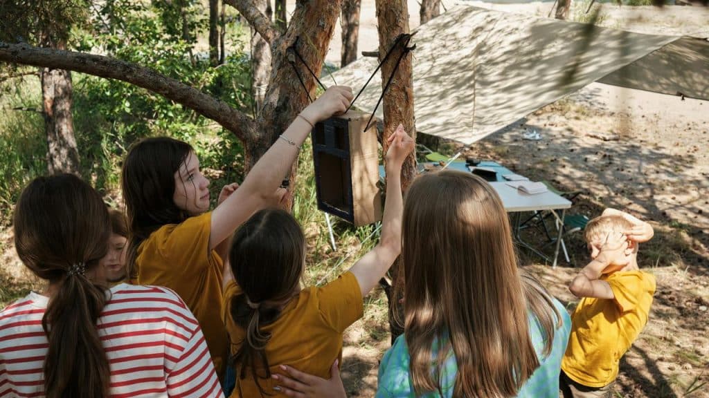 A group of kids hanging a box on a tree at a campsite.