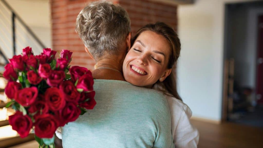 A woman happily hugging someone holding a bouquet of roses.