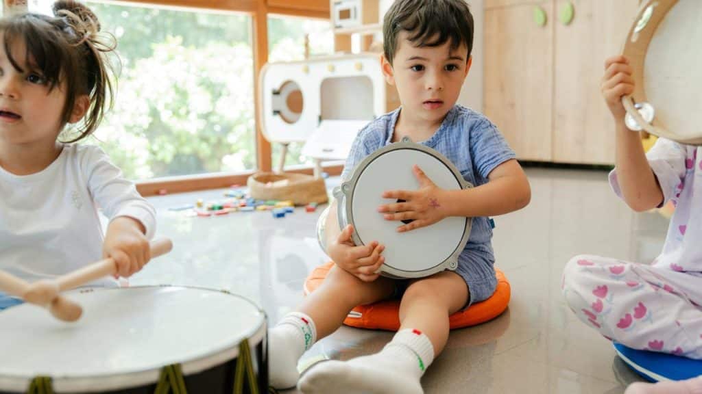 A group of children playing drums and tambourines indoors.