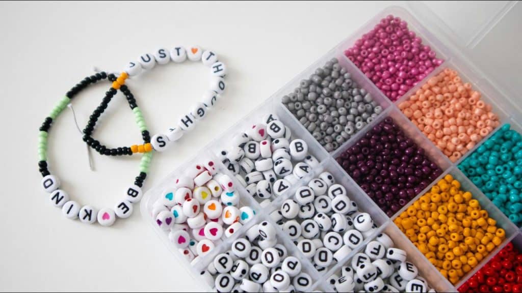 A bead organizer with colorful and lettered beads beside two handmade bracelets.